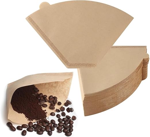 Angled view of a stack of brown unbleached cone coffee filters, with one filter open containing ground coffee and whole roasted coffee beans.