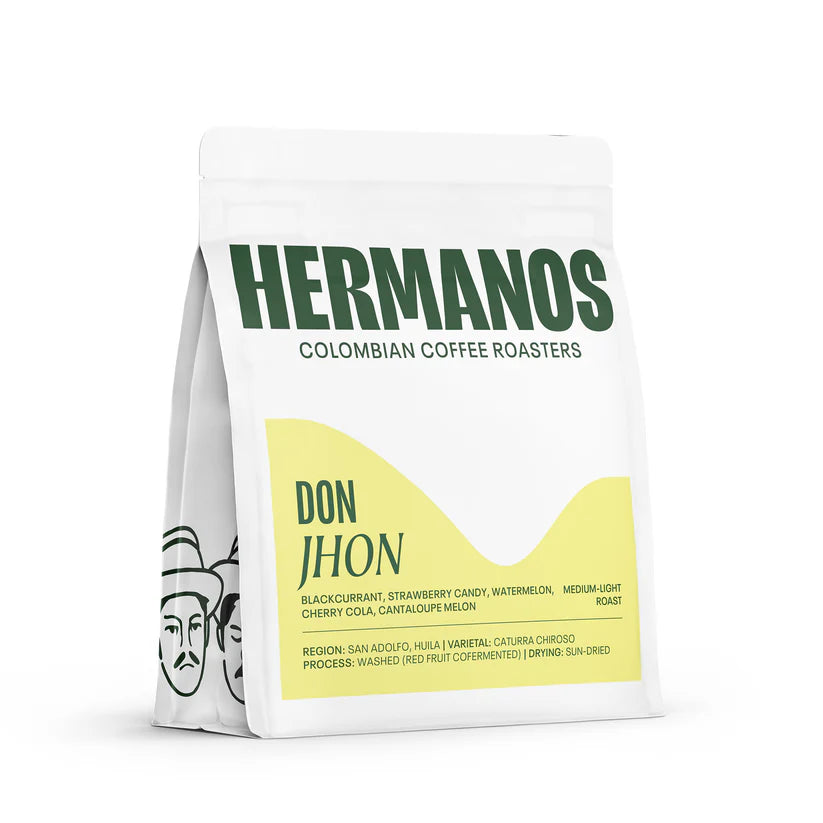 Angled view of a white Hermanos Colombian Coffee Roasters bag featuring a yellow label for the "Don Jhon" medium-light roast specialty coffee.